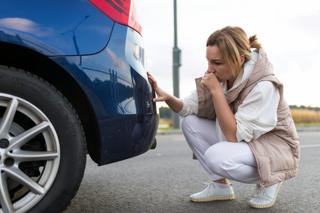 puzzled and annoyed woman looking at scratch on car bumper after minor accident